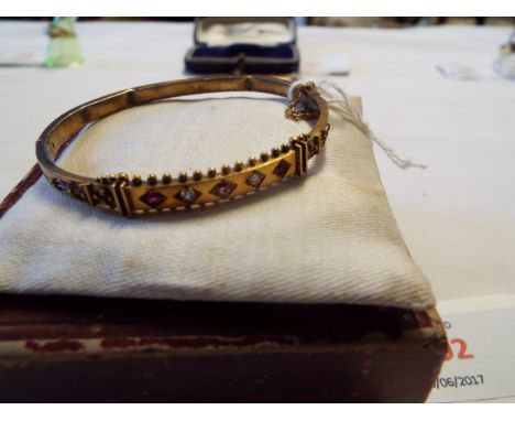 A Victorian yellow metal hinged bangle in Etruscan design with central panel set with alternating diamonds and rubies, the sh