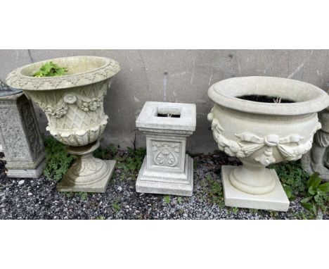 A reconstituted stone urn shaped planter decorated with swags of flowers together with  another decorated with swags of fruit