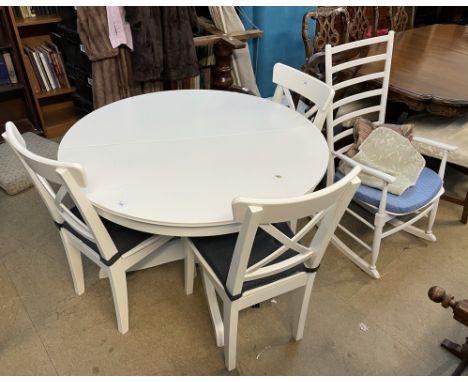 A modern extending dining table in white on a single pedestal together with a set of three dining chairs and a ladder back ro