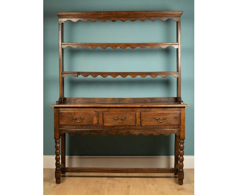 An antique oak dresser with plate rack above with a base with three drawers and standing on bobbin turned legs united by an H