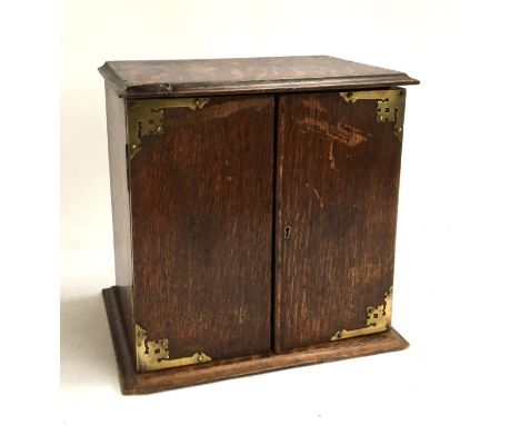 A 19th century oak smoker's cabinet, with brass mounts opening to reveal an arrangement of drawers and pipe rack, some repair