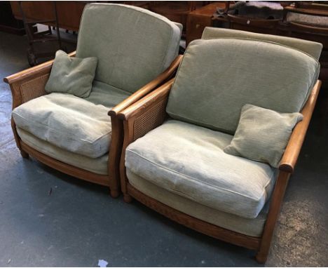 A pair of Ercol light oak bergere armchairs, each with caned sides, upholstered in green fabric, each 90cmW 