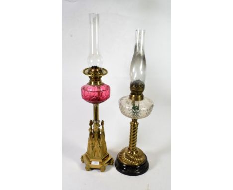 A Victorian brass oil lamp with castellated base and cranberry shade; together with another oil lamp with wrythen and gadroon