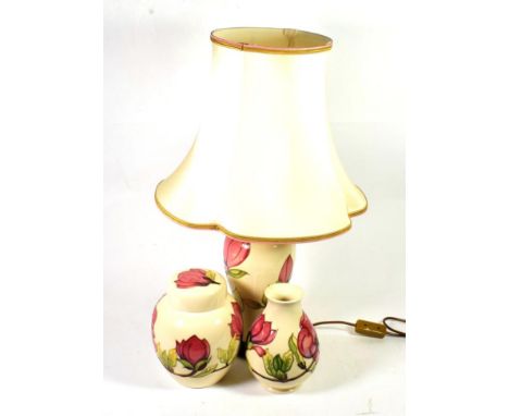 A Moorcroft pottery Magnolia pattern table lamp on a cream ground together with a vase and ginger jar and cover of the same d