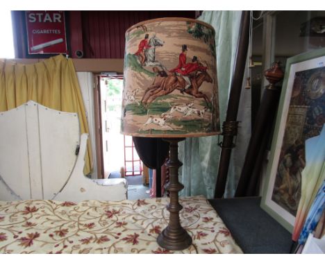 A heavy brass candlestick converted into a lamp with linen shade depicting a hunting scene of men in red jackets, horses and 