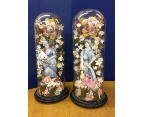 A pair of glass domes containing ceramic fishers and floral surrounds