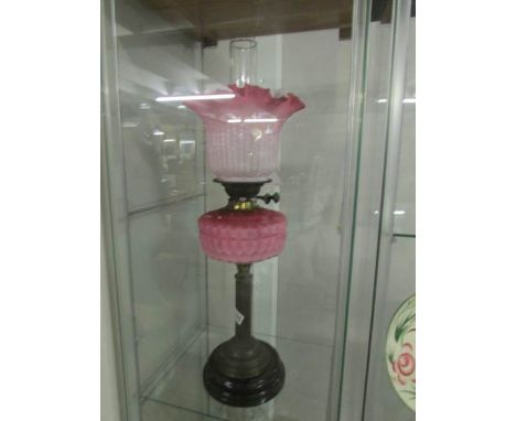 A brass oil lamp with pink glass font and shade.