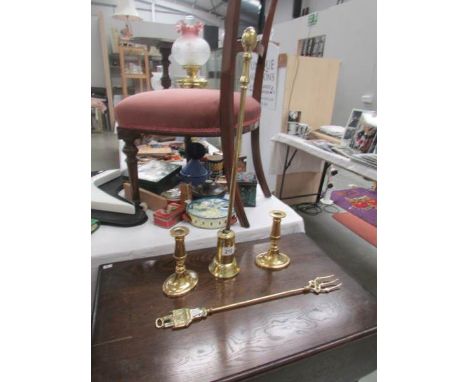 A brass poker in stand, a pair of brass candlesticks and a brass toasting fork.