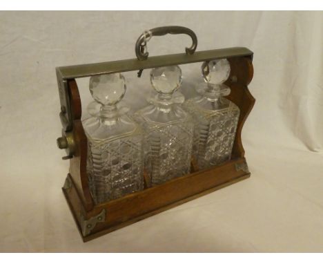 A Betjemann's patent three-bottle tantalus in oak stand with silver plated mounts and key (one decanter chipped)