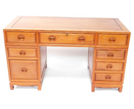 An Oriental hardwood desk, with a paneled top above an arrangement of nine drawers, each with recessed carved handles, on bra