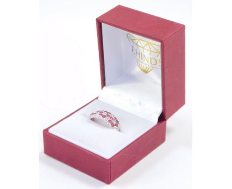 An 18ct white gold ruby and diamond ring, formed as three flower heads, interspersed with pairs of diamonds, size M/O, 5.0g.