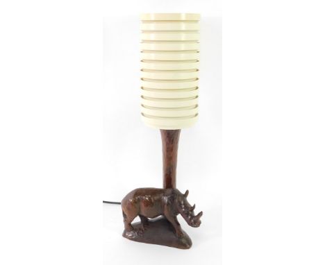 A mid century wooden table lamp carved with a rhinoceros, with a banded cream plastic cylindrical shade, 58cm high.