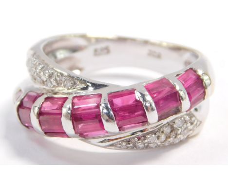 A ruby and diamond crossover ring, set with twenty one baguette cut rubies in white metal, stamped 585, size M, 4.7g.
