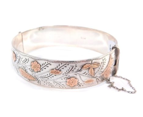 A silver and rose gold plated bangle, engraved and embossed with a bird, butterfly, flowers and leaves, on a snap clasp, with