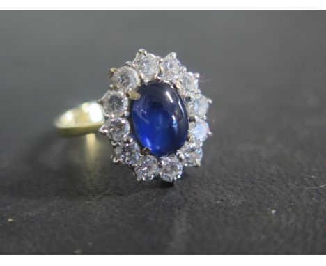 An 18ct yellow and white gold cluster ring, set with a large cabochon sapphire approx 10mm x 8mm surrounded by 12 diamonds, e