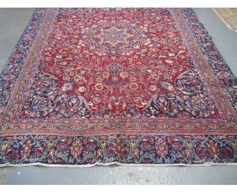 Large Middle Eastern design carpet on a red and blue ground with central floral and foliate medallions, the borders all with 