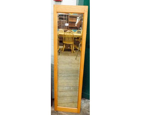 A long bevelled dressing mirror in light oak frame 