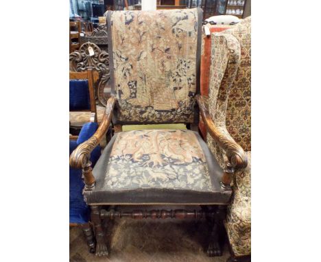 An antique oak framed elbow chair standing on paw feet with tapestry upholstered seat and back 