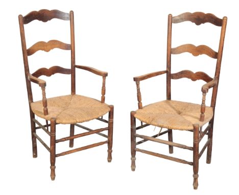 A PAIR OF FRENCH PROVINCIAL OAK RUSH SEAT ARMCHAIRS the ladder back over a rush seat, on turned legs and conforming stretcher