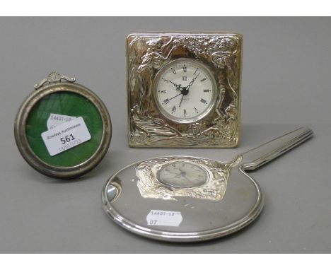 A silver hand mirror, a silver frame and a silver plated clock. The latter 11 cm high.