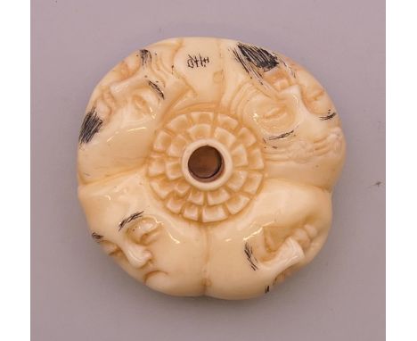 A bone netsuke carved with faces. 4 cm diameter.