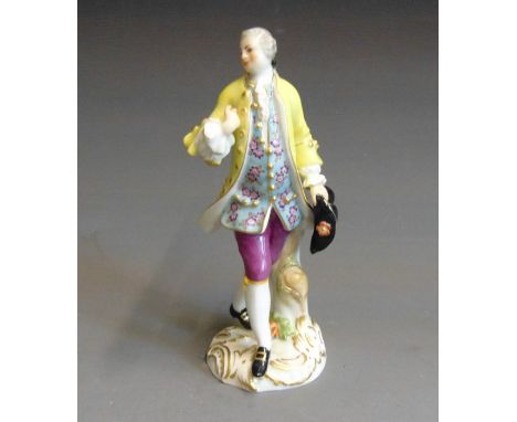 A  Meissen figure of a Gallant striking a pose, dressed in a floral dress coat and bright yellow outer coat holding his hat i