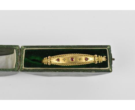 A Victorian yellow metal bangle inset with diamonds and rubies, with twisted textured metal framing and detail, with safety c