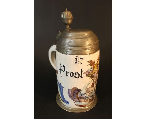 A German ceramic tankard with pewter lid and stand, painted with coat of arms and described „Prost Freund„ and dated 1765; gl