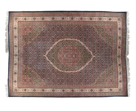 A LARGE PERSIAN WOOL CARPET 20TH CENTURY, woven in red, navy and cream tones with the centre field filled with oval lozenges,