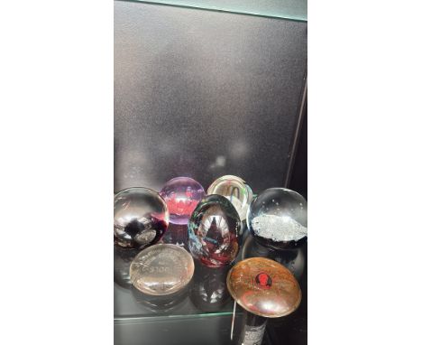 Collection of vintage and contemporary glass paperweights, featuring vibrant colors, controlled bubbles, and abstract designs