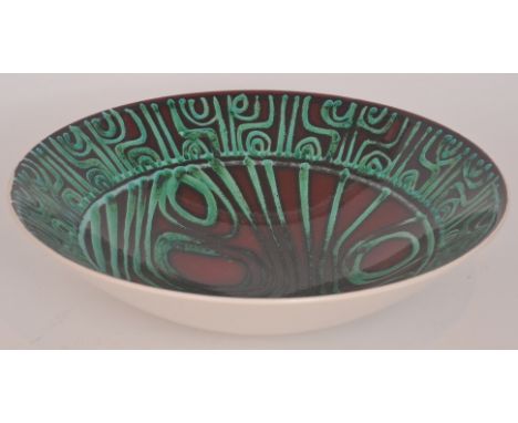 A Poole Pottery Delphis bowl decorated with copper green Aboriginal motifs against a dark red ground, printed marks, diameter