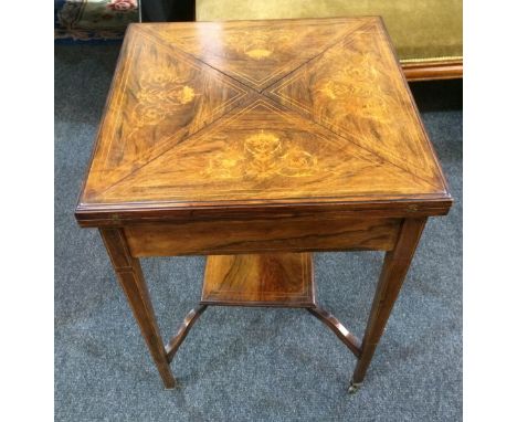 An early 20th Century rosewood veneered envelope top card table with foliate inlaid detail, over a single frieze drawer and l