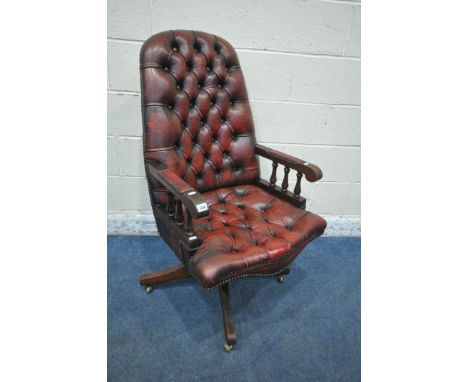 AN OXBLOOD BUTTONED SWIVEL OFFICE CHAIR, with spindled armrests, on brass castors, width 60cm x depth 68cm x height 113cm, co