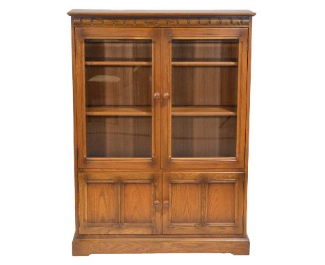 Ercol mid-elm two door bookcase, two glazed doors enclosing shelves, over panelled doors, bracket feet, width 101cm, depth 30