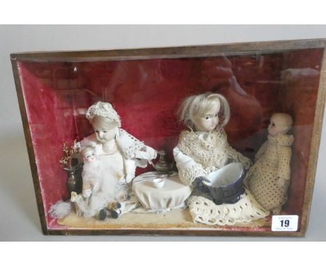 A cased and glazed diorama, depicting mothers feeding their children, containing four bisque head dolls of varied size, with 