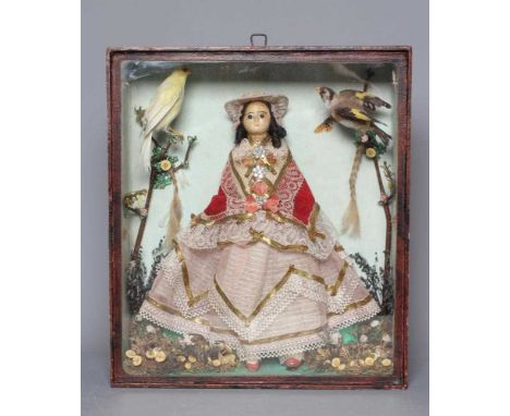 A wax head doll and taxidermy diorama, the doll with moulded and painted features, brown glass fixed eyes, brown wig and lace