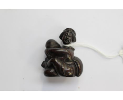 A Japanese dark wood carved Netsuke, depicting a traditionally dressed Japanese woman, holding an oversized penis, signed to 