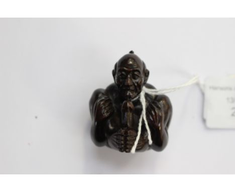 A Japanese dark wood carved Netsuke, depicting an Oriental man in an explicit position, signed to the base 