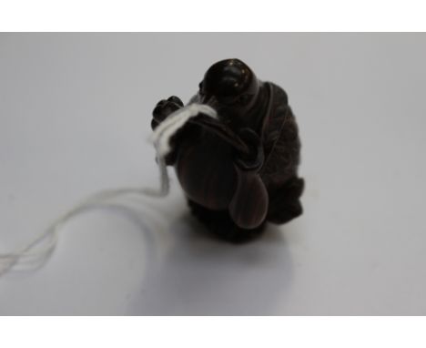 A Japanese dark wood carved Netsuke depicting a Bird with a twig with berries in it's beak, signed to the base 