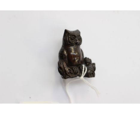 A Japanese dark wood carved Netsuke, depicting an Owl sitting on a gnarled branch, signed to the base 
