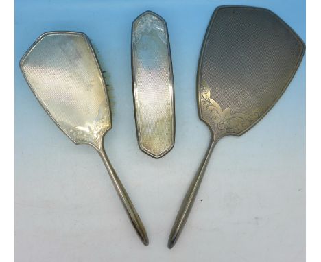 A three piece silver dressing table set, hand mirror and two brushes