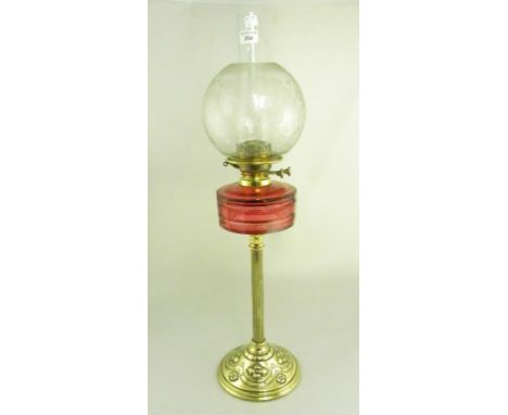 AN EDWARDIAN EMBOSSED BRASS OIL LAMP WITH CRANBERRY GLASS FOUNT AND ETCHED GLASS SHADE