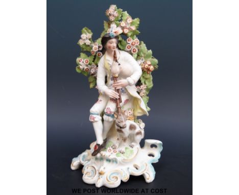 An 18thC Derby patch figure of a piper and his dog on a rococo base,  probably 'Northumbrian Pipes' (21cm tall)