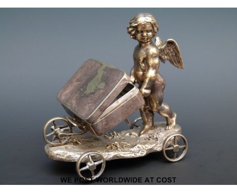 A Elkington & Co. silver plated table snuff box, supported on a wheelbarrow being moved by a cherub, all on a wheeled base, h