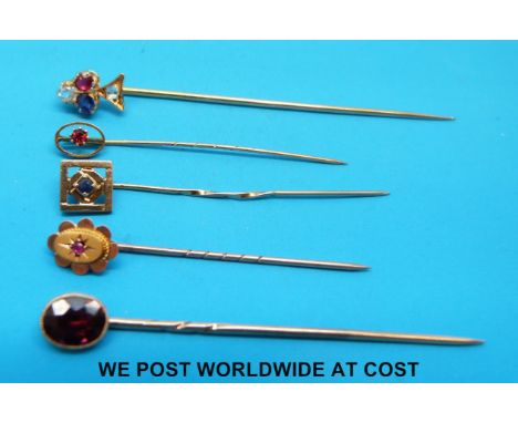 Three yellow metal stick pins, one set with a sapphire, one ruby and the other garnet, all marked 9ct, together with two yell