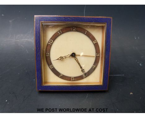 An Art Deco travel alarm clock with blue enamel Greek key border, bevelled glass, Deco chapter ring and folding brass stand t