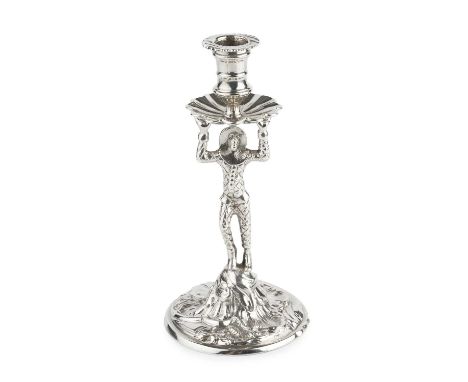 A George II silver taper stick, the nozzle with fluted drip tray supported by a standing Harlequin, on circular foliate scrol