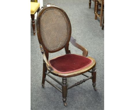 A Victorian nursing chair, oval wickerwork back, padded seat, turned supports and stretchers, ceramic castors