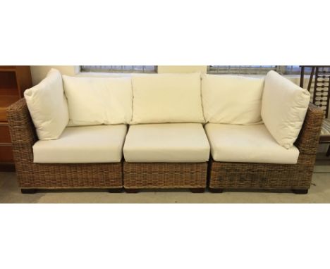 A cane 3 sectional conservatory sofa with plush cream cushions.
