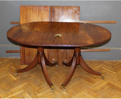 A George III style mahogany two pillar dining table having a reeded border, raised on swept legs including two extra leaves, 